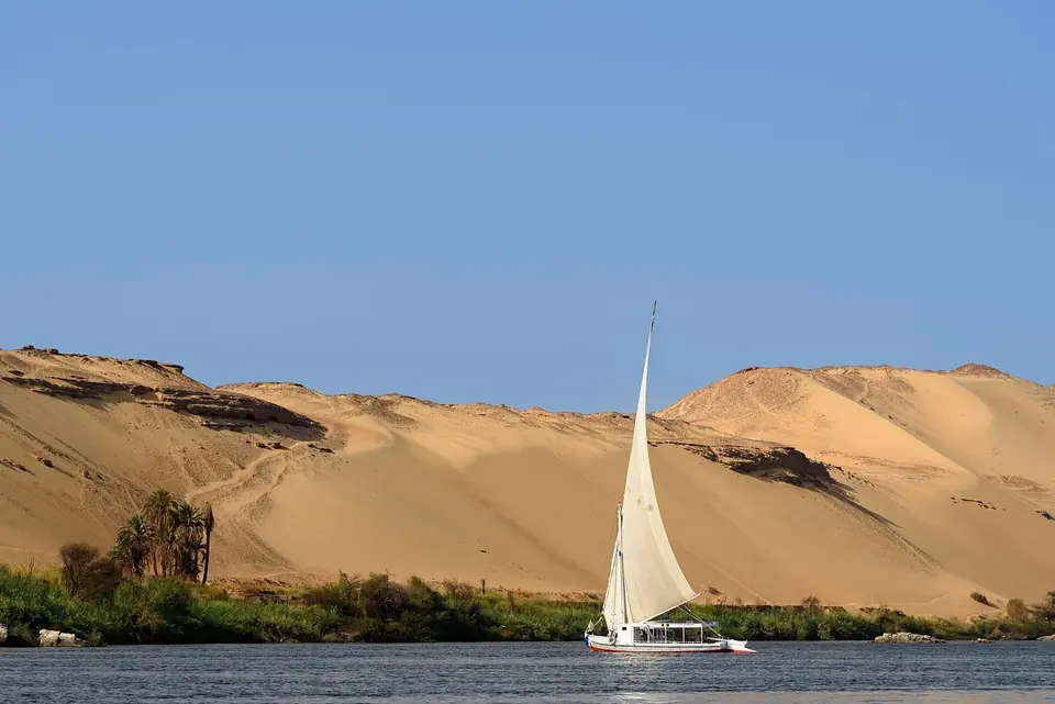 Falua de vela branca no rio Nilo junto a dunas de areia